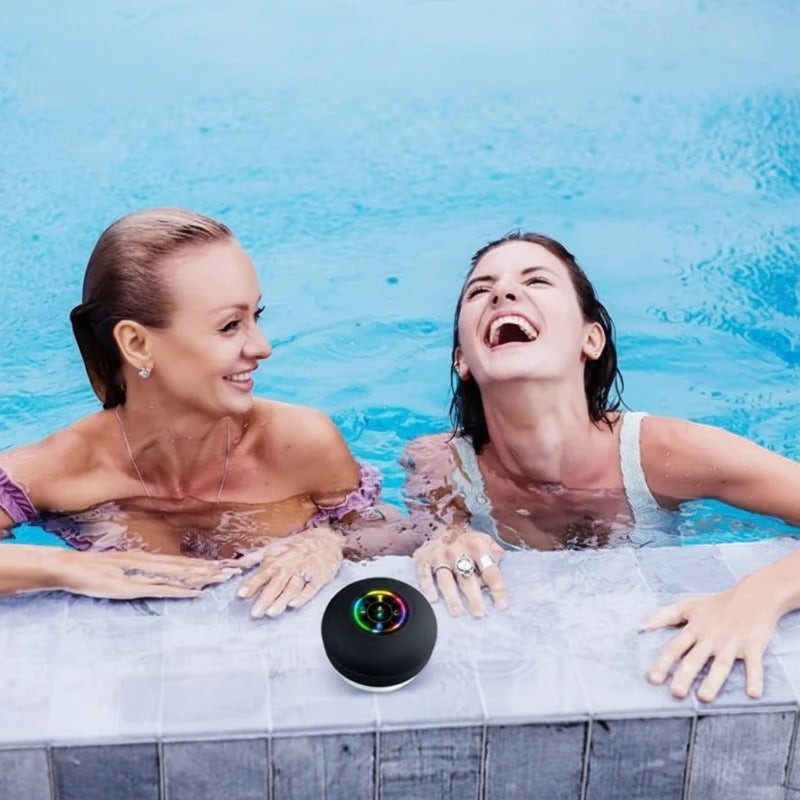 Nova Haus Sonic-Grip black waterproof Bluetooth speaker with LED lights, poolside with two women laughing in the water.